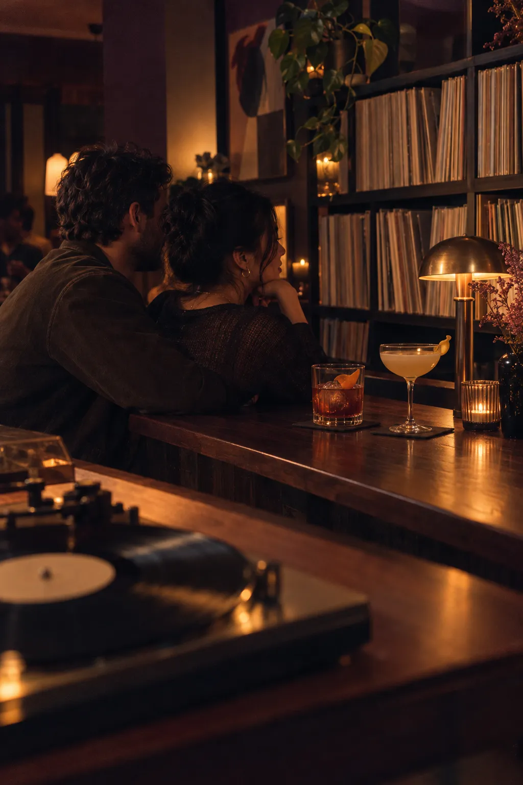 Two cocktails on a walnut bar beside a turntable and shelves of records